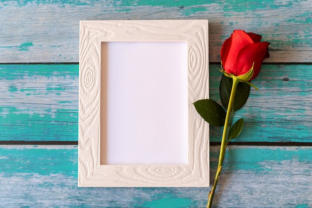 Cornice in bianco e rose rosse sopra la tavola di legno