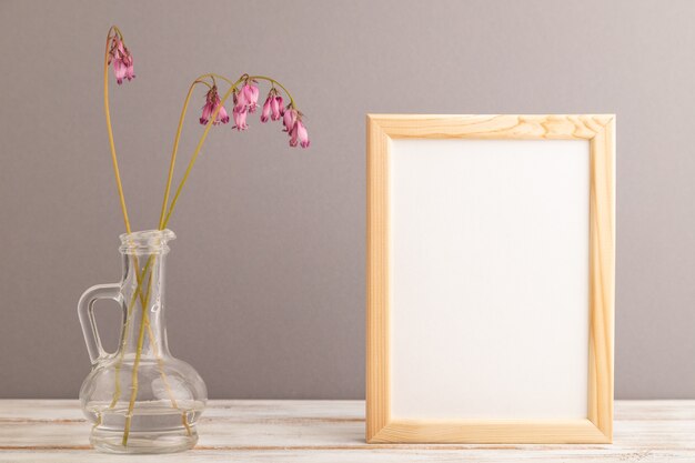 Cornice in legno con dicentra rosa, cuore spezzato in vetro su sfondo grigio pastello. vista laterale