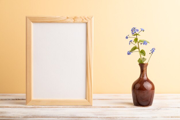 cornice in legno con fiori blu del nontiscordardime in vaso di ceramica su sfondo arancione pastello. vista laterale,