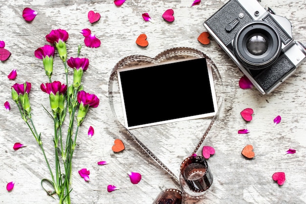 Cornice per foto in bianco nel film a forma di cuore con retro macchina fotografica e fiori di garofano