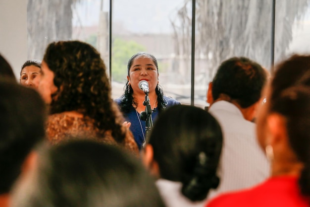 Coro femminile che canta in mezzo a un pubblico di uomini e donne.