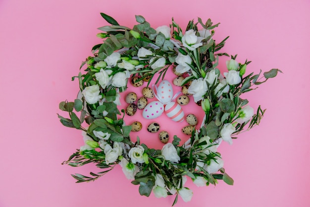 Corona con rose bianche e uova di Pasqua su sfondo rosa. Decorato. Sopra la vista