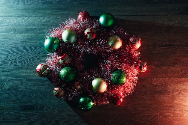 Corona di Natale di ghirlande rosse e giocattoli di Natale sul di un tavolo di legno. Buon Natale e buone feste. Vista dall'alto