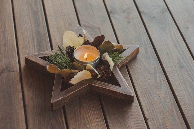 Corona di natale in un vassoio della stella con una candela. Splendide decorazioni in stile rustico su un tavolo di legno.