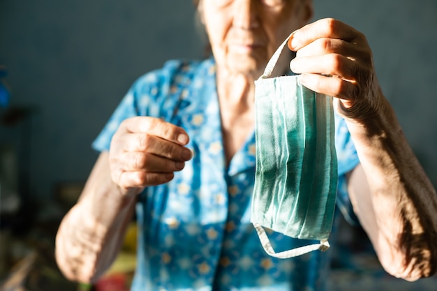 Coronavirus, donna mascherata, 86 anni con in mano una maschera protettiva contro il coronavirus. vecchia che indossa una maschera per il viso