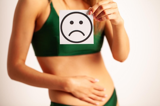 Corpo femminile di salute della donna in bikini che tiene la carta di sorriso triste vicino al problema di salute della donna dello stomaco e al mens