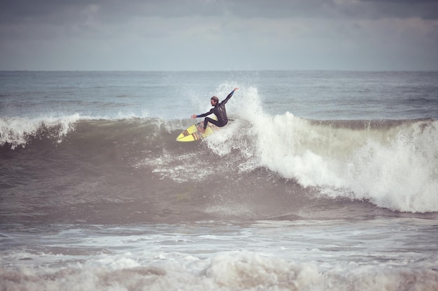 Corpo intero di surfista maschio in piedi sulla tavola da surf che cattura l'onda e cavalca l'onda mentre si gode un hobby estremo nell'oceano