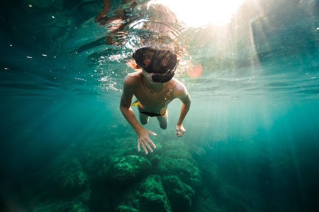 Corpo pieno di giovane subacqueo maschio senza camicia in maschera per lo snorkeling che esplora l'oceano blu durante le immersioni in giornata di sole