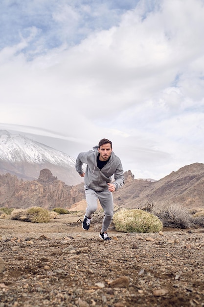 Corpo pieno di uomo barbuto in abbigliamento sportivo e scarpe da ginnastica in esecuzione su un terreno pietroso vicino al vulcano di Teide a Tenerife nelle Isole Canarie in Spagna