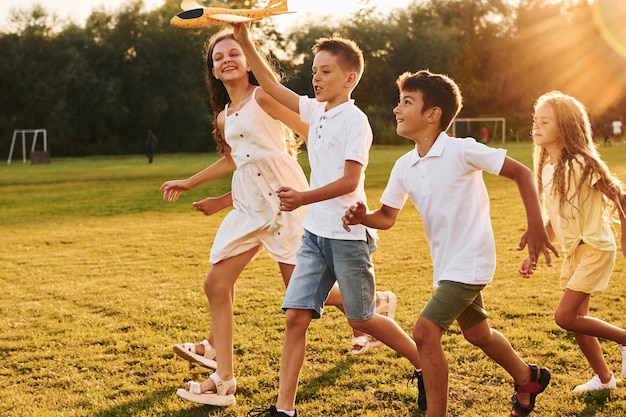 Correre con l'aereo giocattolo Un gruppo di bambini felici è all'aperto sul campo sportivo durante il giorno