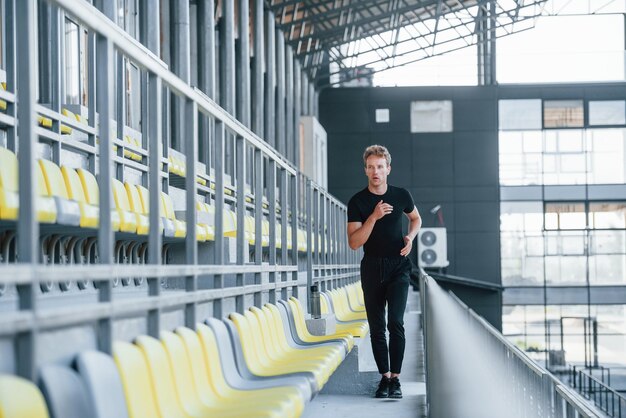 Correre sulle gradinate Giovane sportivo in camicia nera e pantaloni all'aperto durante il giorno