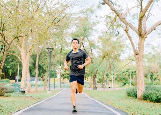 Corridore asiatico sano felice dell'uomo che corre all'aperto nel parco al mattino