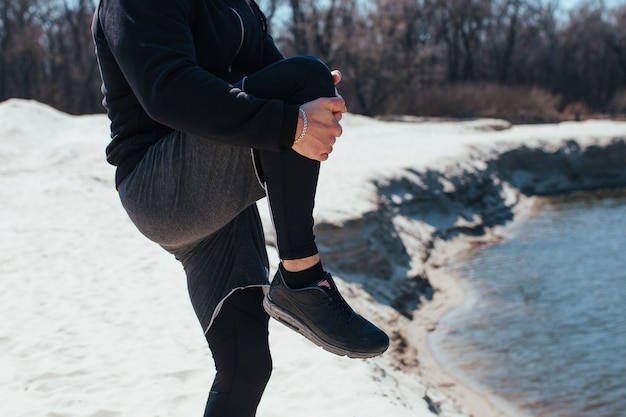 Corridore dell'atleta che allunga le sue gambe prima dell'allenamento nella natura