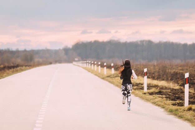 Corridore della donna in abiti sportivi sulla strada vuota a figura intera