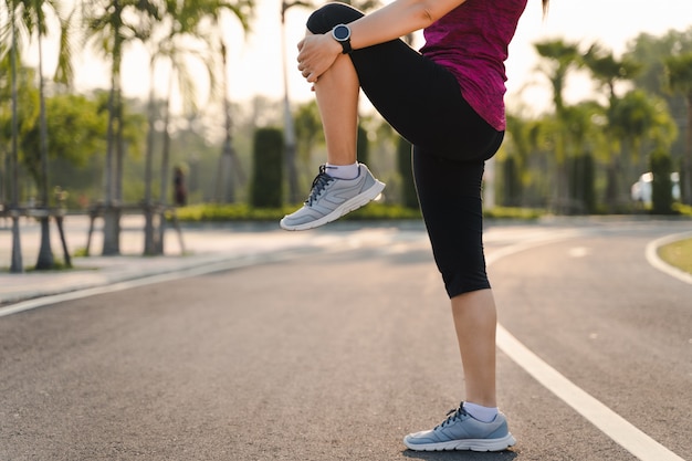 Corridore della giovane donna che allunga le gambe prima dell'esecuzione nel parco.