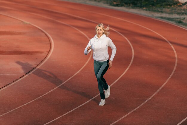 Corridore femminile caucasico in abiti sportivi in esecuzione sullo stadio con le cuffie nelle orecchie.