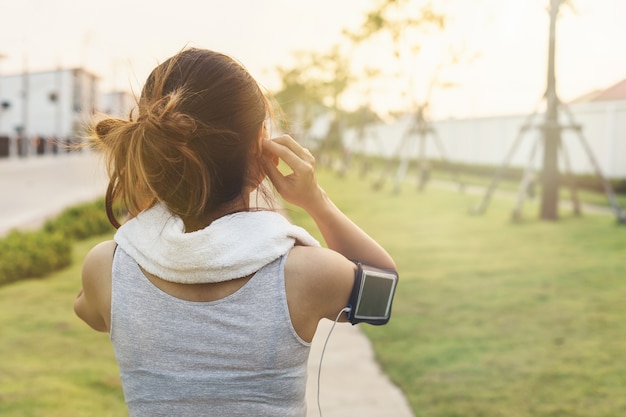 Corridore femminile che pareggia e che utilizza smartphone per ascoltare musica nel parco, allenamento all&#39;aperto