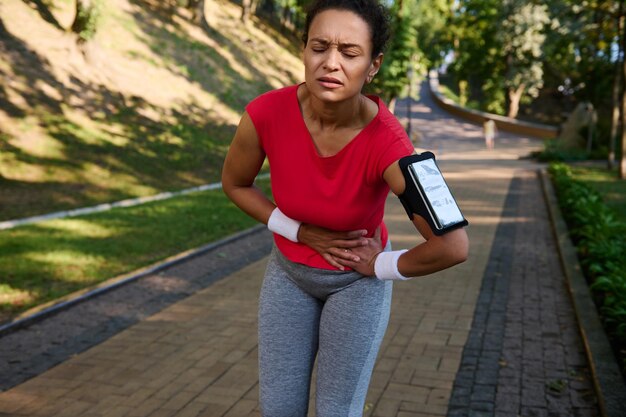 Corridore femminile che sente esaurimento e crampi laterali mal di stomaco durante la corsa nel parco cittadino Concetto di stile di vita attivo sano lesioni sportive