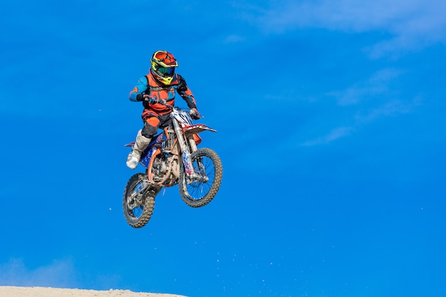 Corridore su una moto in volo, salta e decolla su un trampolino contro il cielo.