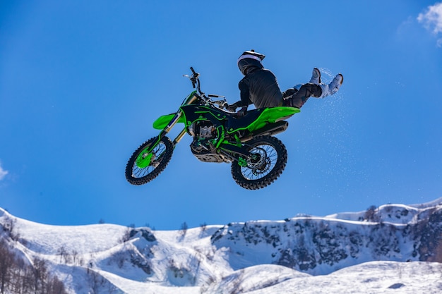 Corridore su una moto in volo, salta e decolla su un trampolino contro le montagne innevate