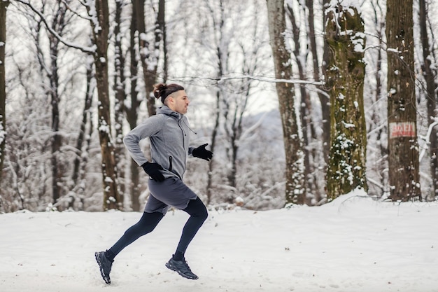 Corridore veloce che corre nella foresta il giorno di inverno nevoso. Stile di vita sano, fitness invernale