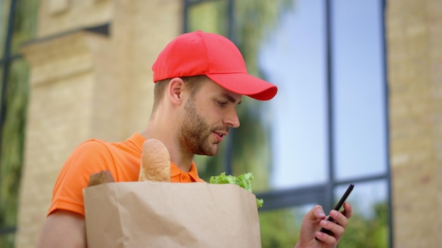 Corriere che utilizza il telefono cellulare per cercare l'indirizzo Uomo che consegna cibo in borsa