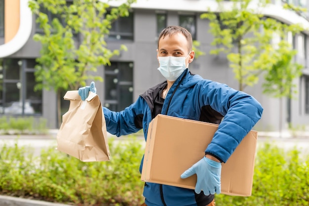 Corriere di consegna postale uomo che indossa una maschera protettiva davanti al furgone da carico che consegna la scatola di contenimento del pacco a causa della malattia di Coronavirus o COVID-19.