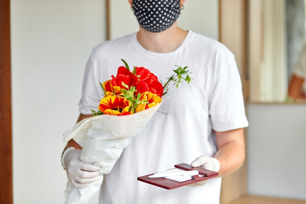 Corriere, fattorino in guanti medici in lattice consegna in sicurezza acquisti online un mazzo di fiori