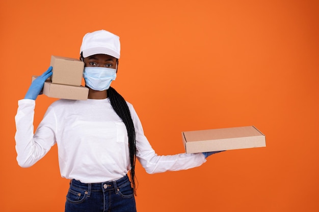 Corriere femminile afroamericano che indossa una maschera protettiva contro il virus e un cappuccio bianco con in mano un pacco