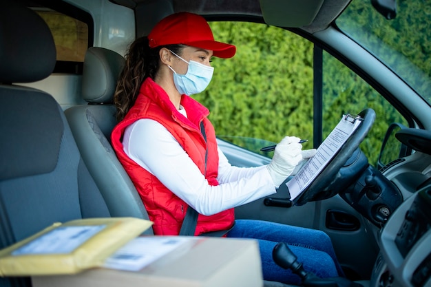 Corriere femminile con maschera di protezione che consegna la spedizione durante la pandemia del virus corona