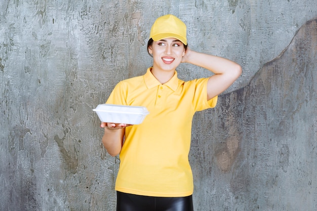 Corriere femminile in uniforme gialla che consegna una scatola bianca da asporto e sembra premuroso.