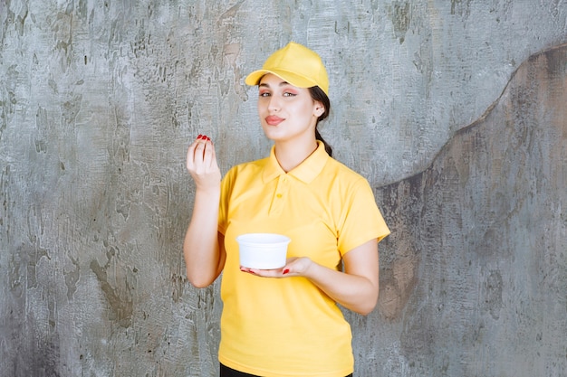 Corriere femminile in uniforme gialla che tiene una tazza da asporto e si gode il prodotto