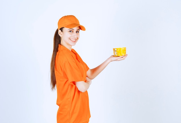 Corriere femminile in uniforme gialla che tiene una tazza di noodles da asporto.