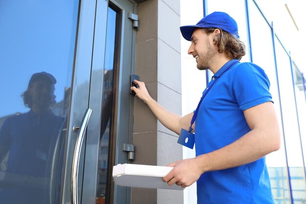 Corriere maschio con pizza che suona nel campanello all'ingresso Servizio di consegna cibo