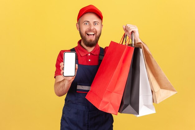 Corriere uomo che tiene cellulare e borse della spesa che fa pubblicità al negozio online sul dispositivo mobile