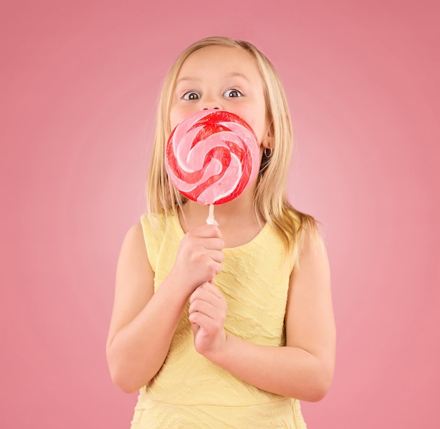 Corsa di zucchero caramellato e lecca-lecca con ragazza in studio per dolci festa e cibo di carnevale isolato su sfondo rosa Carino eccitato e giovane con bambino e mangiare spuntino colorato per giocoso e trattare