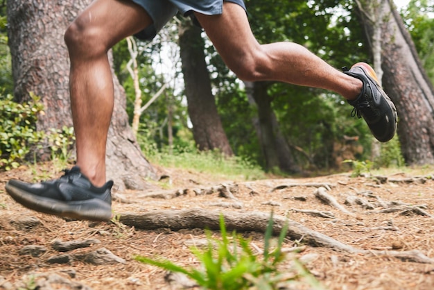 Corsa fitness e gambe di un uomo nella foresta per esercizi di maratona e allenamento cardio Natura sportiva e piedi di un atleta nei boschi per il benessere di corpo e muscoli sani per la gara o la sfida
