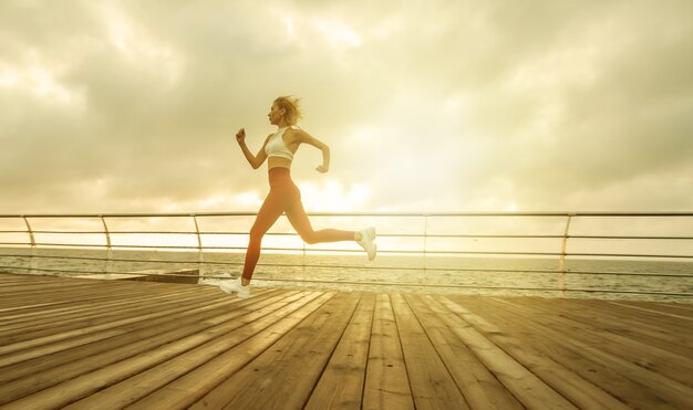 Corsa mattutina. Giovane donna atletica in abiti sportivi corre sulla spiaggia all'alba. Allenamento all'aperto. Uno stile di vita sano. Sprint