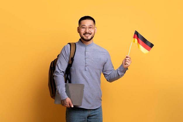 Corsi di lingua online sorridente giovane uomo asiatico con bandiera tedesca e laptop