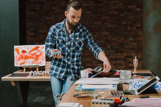 Corso di formazione artistica online Autoeducazione Giovane uomo che guarda il video tutorial su tablet utilizzando vernice acrilica per le sue opere d'arte