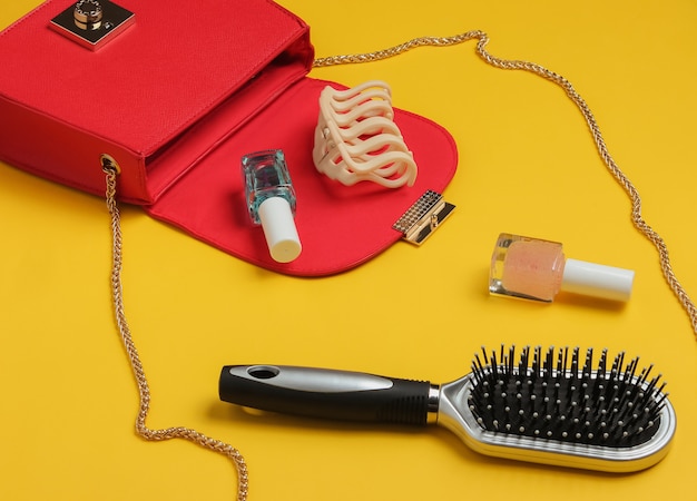 Cosa c'è nella borsa delle donne Borsa in pelle rossa con prodotti cosmetici accessori da donna su sfondo giallo