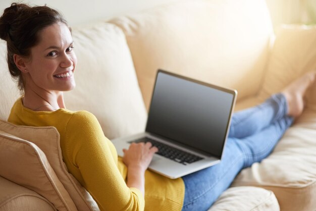 Cosa ne pensi del mio blog Foto di una giovane donna attraente che usa il suo laptop sul divano di casa