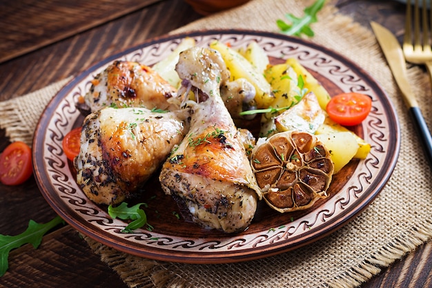 Cosce di pollo al forno con patate a fette ed erbe aromatiche. Cosce di pollo barbecue sulla tavola di legno.