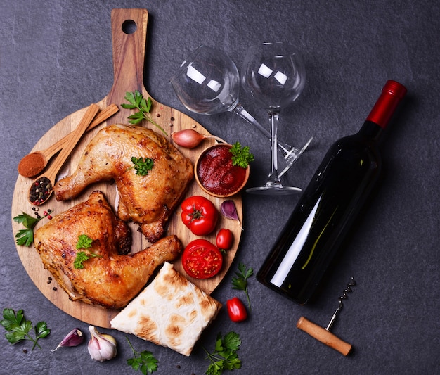 Cosce di pollo alla griglia con spezie e verdure, con una bottiglia di vino rosso.