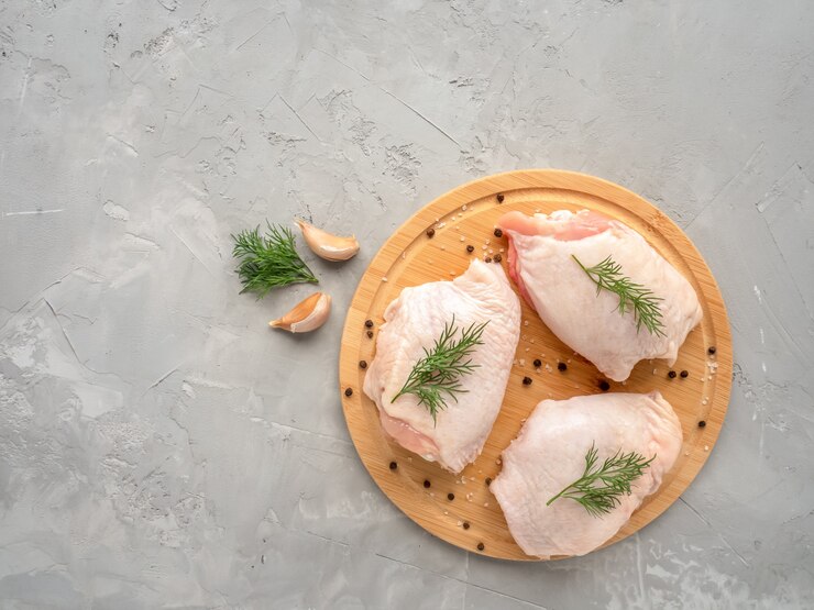 Cosce di pollo crude sul tagliere con ingredienti per cucinare al tavolo da cucina in cemento grigio. Vista dall'alto con copia spazio.