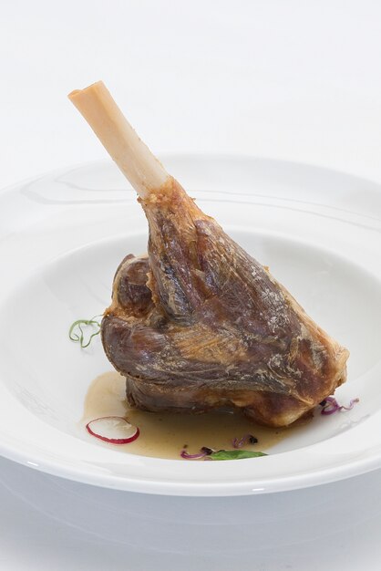 Coscia di agnello arrosto, servita con salsa bianca, decorata con erbe aromatiche