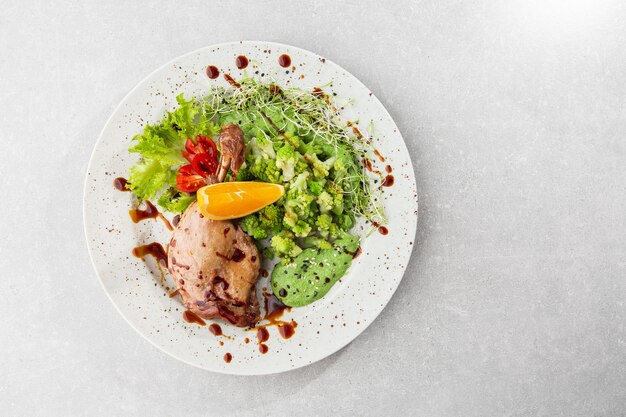 Coscia di anatra arrosto con broccoli romanesco al forno, fetta di limone e peperoncino sul piatto bianco