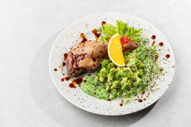 Coscia di anatra arrosto con broccoli romanesco al forno, fetta di limone e peperoncino sul piatto bianco