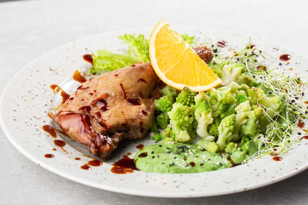 Coscia di anatra arrosto con broccoli romanesco al forno, fetta di limone e peperoncino sul piatto bianco