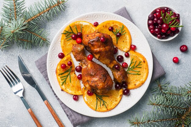 Coscia di pollo al forno con arance e mirtilli rossi in una luce targa. Tabella dell'alimento di natale con le decorazioni.